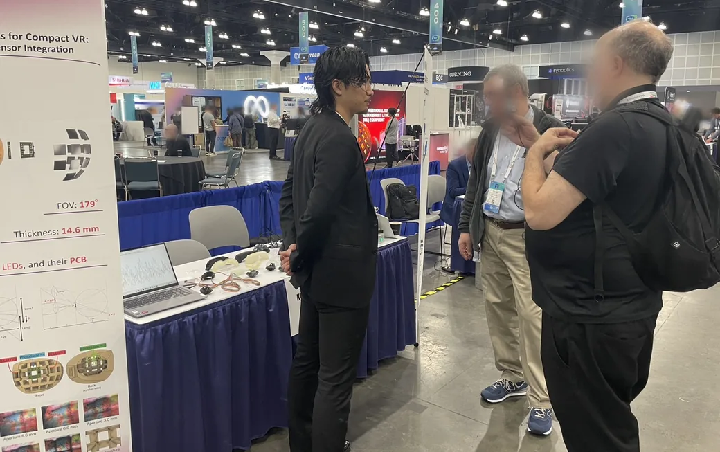 The Cyrisin booth at the I-Zone of SID Display Week 2026. The poster lists a 179° field of view and 14.6 mm optical thickness, and a visitor is trying the prototype HMD on.